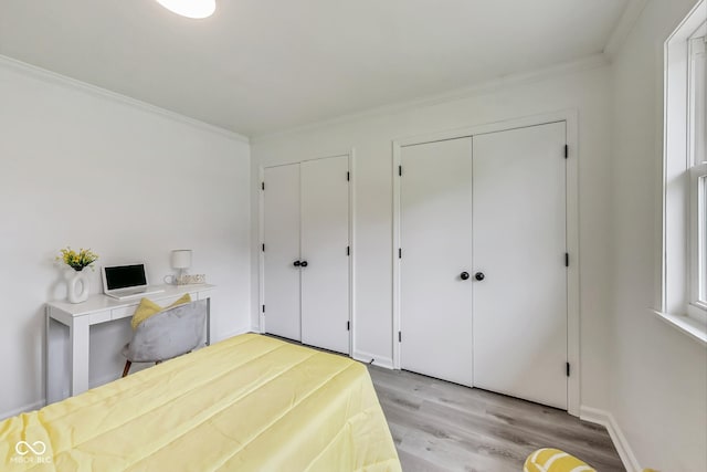 bedroom featuring ornamental molding, multiple closets, and light wood-type flooring