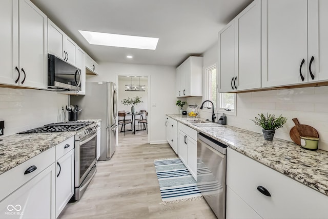 kitchen with sink, white cabinetry, a skylight, stainless steel appliances, and light hardwood / wood-style floors