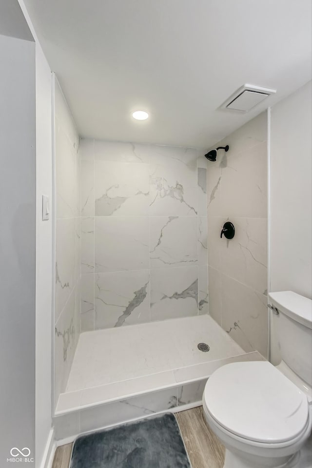 bathroom with wood-type flooring, tiled shower, and toilet