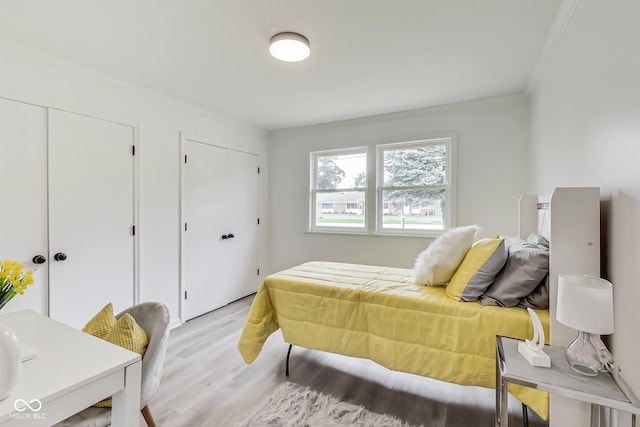 bedroom with crown molding, light hardwood / wood-style flooring, and multiple closets