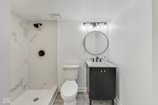 bathroom with vanity, wood-type flooring, a tile shower, and toilet