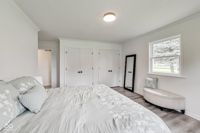 bedroom featuring multiple closets, ornamental molding, and hardwood / wood-style floors