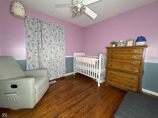 bedroom with ceiling fan, dark hardwood / wood-style floors, and a crib