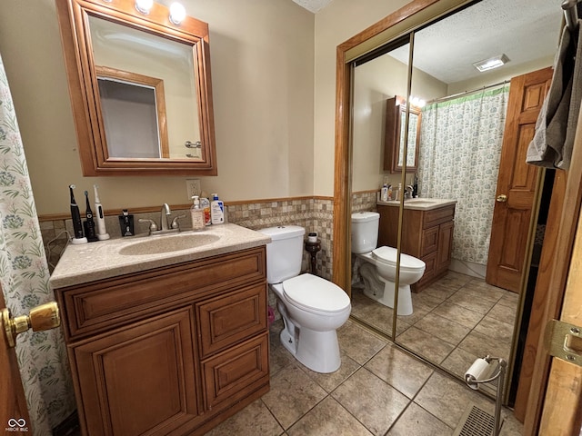 bathroom with tile walls, vanity, toilet, tile patterned floors, and a textured ceiling