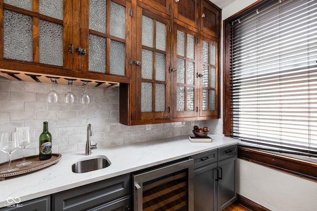 bar with wine cooler, sink, light stone counters, and backsplash