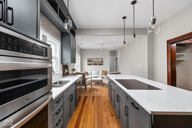 kitchen with pendant lighting, appliances with stainless steel finishes, a kitchen island, and light wood-type flooring