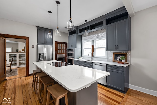 kitchen featuring a kitchen island, appliances with stainless steel finishes, decorative light fixtures, sink, and light hardwood / wood-style floors