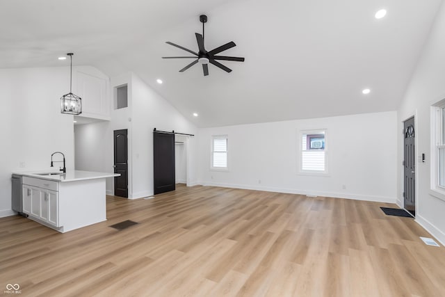 unfurnished living room with ceiling fan with notable chandelier, high vaulted ceiling, sink, a barn door, and light wood-type flooring