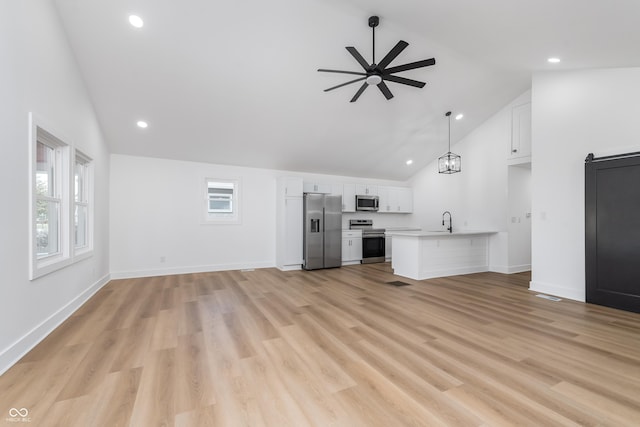 unfurnished living room featuring sink, ceiling fan with notable chandelier, light hardwood / wood-style floors, and high vaulted ceiling