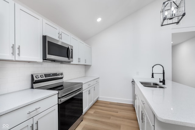 kitchen featuring pendant lighting, sink, appliances with stainless steel finishes, light stone countertops, and white cabinets