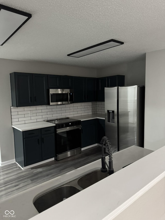 kitchen with appliances with stainless steel finishes, light wood-type flooring, a textured ceiling, and decorative backsplash