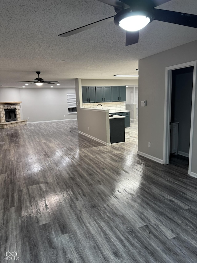 unfurnished living room featuring ceiling fan, a fireplace, dark hardwood / wood-style flooring, and a textured ceiling