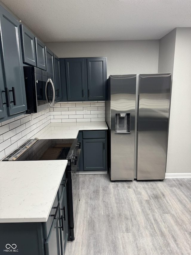 kitchen with backsplash, stainless steel appliances, a textured ceiling, and light wood-type flooring