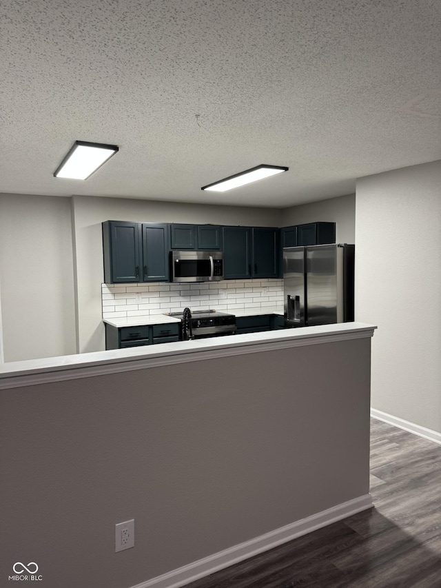 kitchen featuring tasteful backsplash, a textured ceiling, appliances with stainless steel finishes, dark hardwood / wood-style floors, and kitchen peninsula