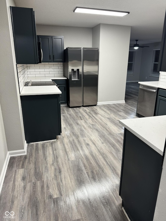 kitchen featuring wood-type flooring, appliances with stainless steel finishes, backsplash, and ceiling fan