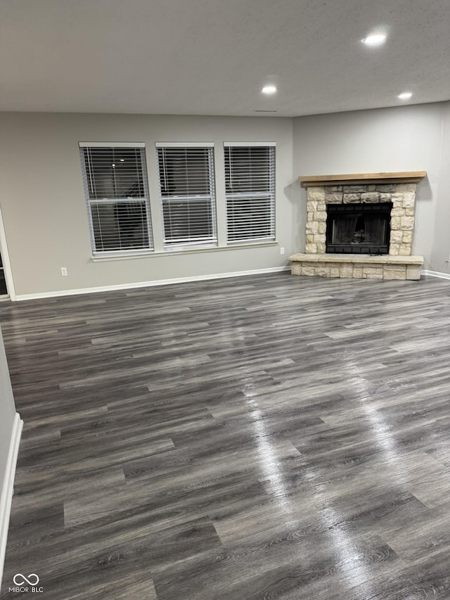 unfurnished living room featuring dark hardwood / wood-style flooring and a stone fireplace