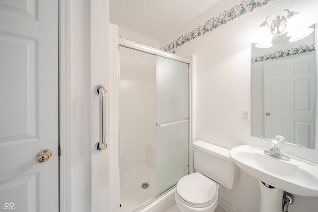 bathroom featuring toilet, a shower with shower door, and sink