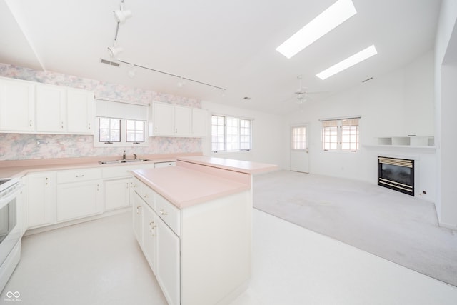 kitchen with sink, a center island, light carpet, a healthy amount of sunlight, and white cabinets