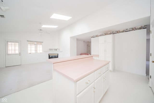 kitchen featuring ceiling fan, vaulted ceiling with skylight, light colored carpet, and white cabinets