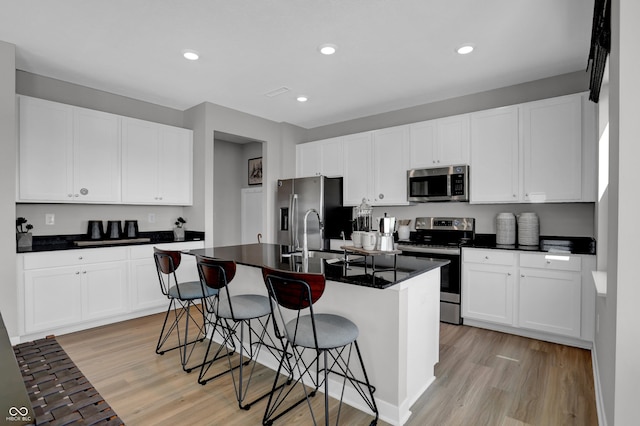 kitchen with sink, a breakfast bar area, stainless steel appliances, white cabinets, and a center island with sink