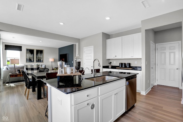 kitchen with an island with sink, dishwasher, sink, white cabinets, and dark stone counters