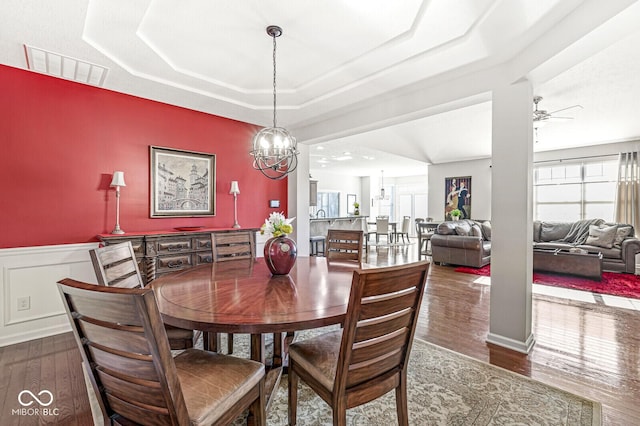 dining area featuring dark hardwood / wood-style floors, ceiling fan with notable chandelier, and a raised ceiling