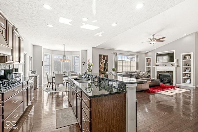 kitchen featuring decorative light fixtures, an island with sink, sink, dark stone countertops, and dark hardwood / wood-style flooring