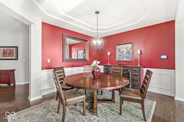 dining space with an inviting chandelier, a tray ceiling, and dark hardwood / wood-style flooring