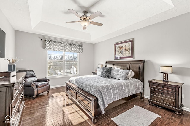 bedroom with a tray ceiling, a textured ceiling, dark hardwood / wood-style floors, and ceiling fan