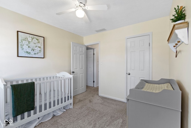 carpeted bedroom featuring a nursery area, a textured ceiling, and ceiling fan