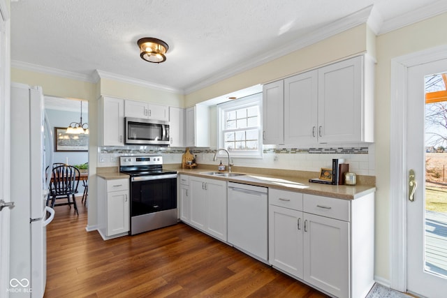 kitchen with appliances with stainless steel finishes, dark hardwood / wood-style floors, white cabinetry, sink, and ornamental molding