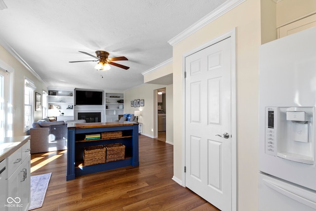 kitchen with white cabinetry, white refrigerator with ice dispenser, ceiling fan, crown molding, and dark wood-type flooring