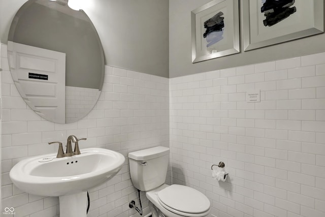 bathroom featuring toilet, sink, and tile walls