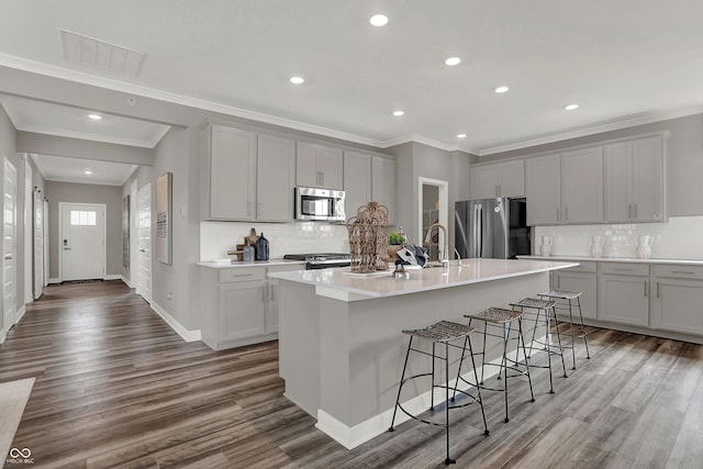 kitchen featuring stainless steel appliances, a kitchen island with sink, a breakfast bar area, and gray cabinetry