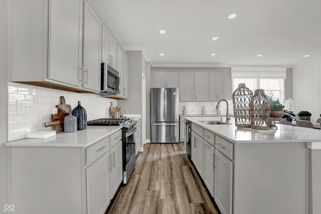 kitchen with sink, light wood-type flooring, appliances with stainless steel finishes, an island with sink, and decorative backsplash