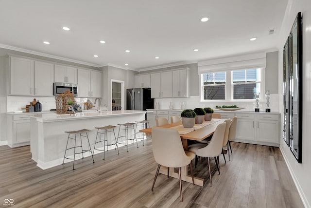 kitchen with light wood-type flooring, stainless steel appliances, a kitchen island with sink, and white cabinets