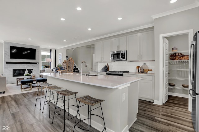 kitchen with a kitchen bar, sink, a center island with sink, ornamental molding, and stainless steel appliances