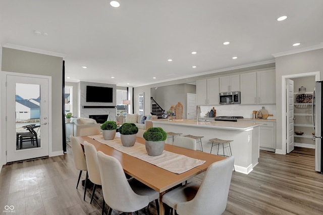 dining area with sink, ornamental molding, a fireplace, and light hardwood / wood-style floors