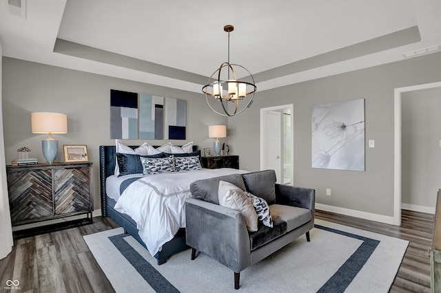 bedroom featuring an inviting chandelier, dark wood-type flooring, and a raised ceiling