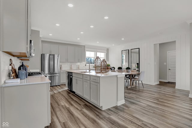 kitchen with appliances with stainless steel finishes, sink, decorative backsplash, a kitchen island with sink, and light wood-type flooring