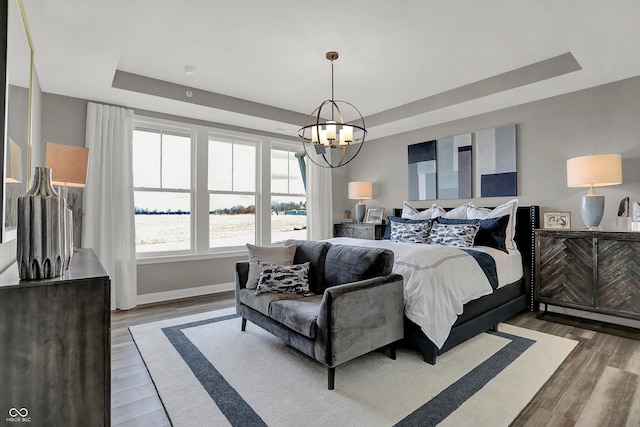 bedroom featuring hardwood / wood-style flooring, a notable chandelier, and a tray ceiling