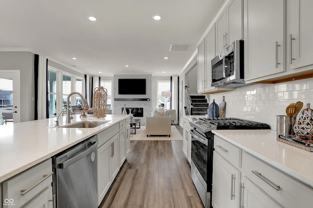 kitchen featuring sink, backsplash, stainless steel appliances, a large fireplace, and white cabinets