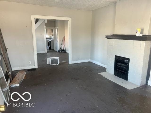 unfurnished living room with a wall unit AC, a textured ceiling, and a fireplace