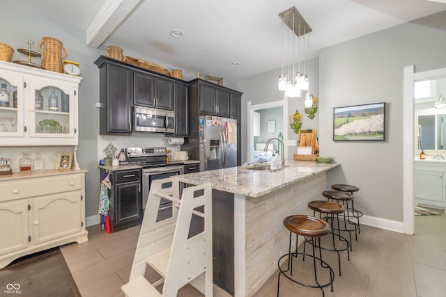 kitchen with sink, backsplash, a kitchen bar, stainless steel appliances, and light stone countertops