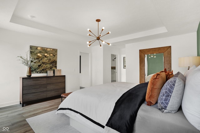 bedroom with light hardwood / wood-style flooring, an inviting chandelier, and a tray ceiling