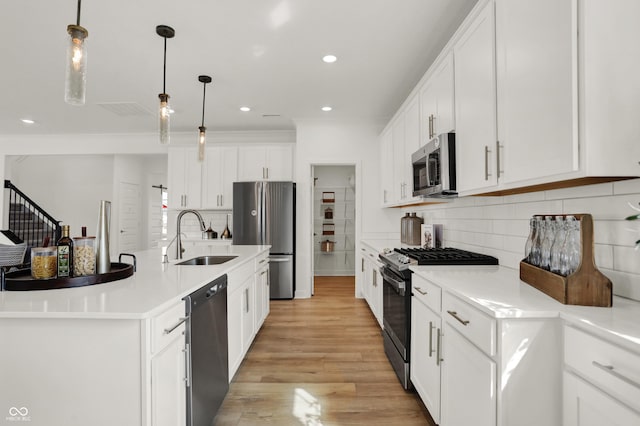 kitchen with sink, an island with sink, pendant lighting, stainless steel appliances, and white cabinets