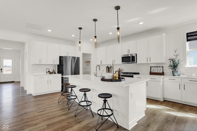 kitchen featuring appliances with stainless steel finishes, decorative light fixtures, a kitchen island with sink, and white cabinets