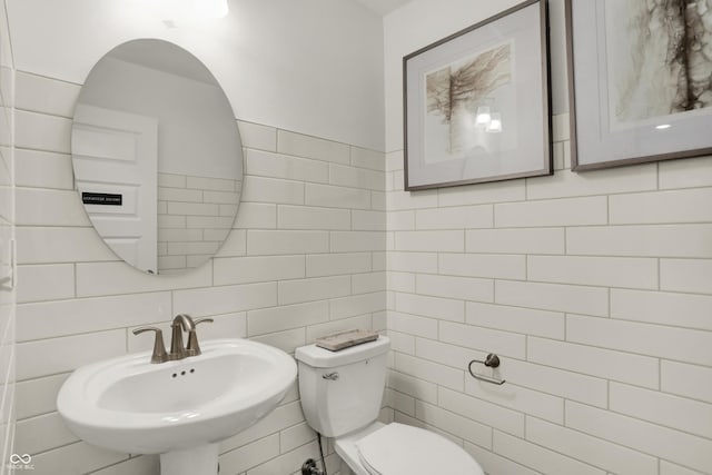 bathroom with toilet, sink, and tile walls