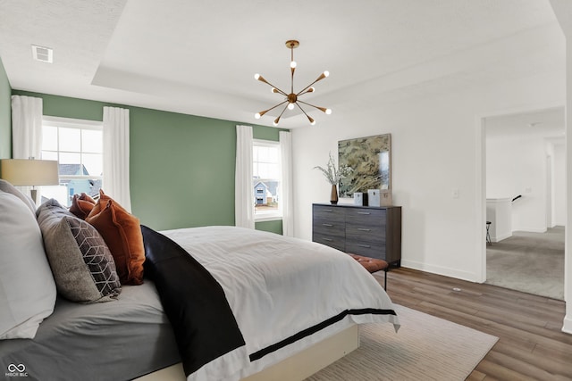 bedroom with multiple windows, hardwood / wood-style flooring, a raised ceiling, and a chandelier