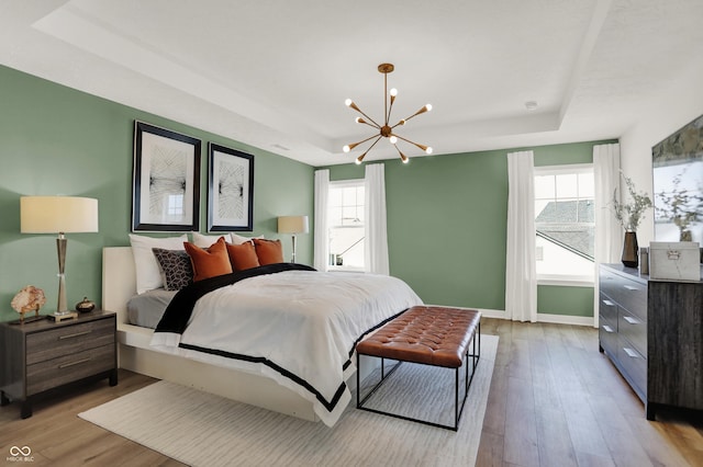 bedroom featuring multiple windows, a tray ceiling, and light hardwood / wood-style floors